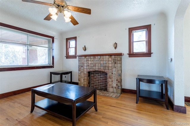 living room featuring ceiling fan, a fireplace, a textured ceiling, and light wood-type flooring