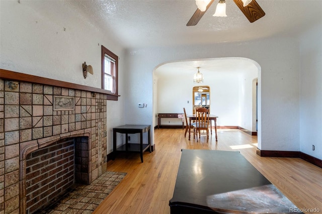 living room with ceiling fan, a fireplace, a textured ceiling, and hardwood / wood-style floors