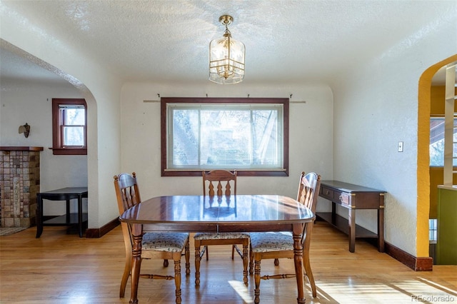 dining space with a healthy amount of sunlight, light wood-type flooring, a notable chandelier, and a textured ceiling