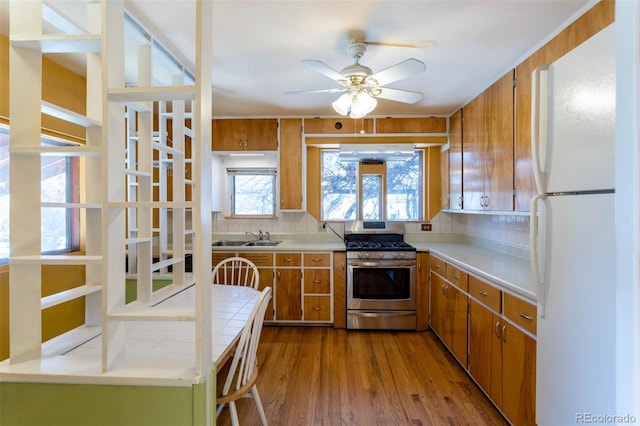 kitchen featuring ceiling fan, tasteful backsplash, white fridge, light wood-type flooring, and stainless steel gas range