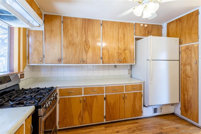 kitchen with white refrigerator, tasteful backsplash, ceiling fan, stainless steel range with gas cooktop, and light hardwood / wood-style flooring