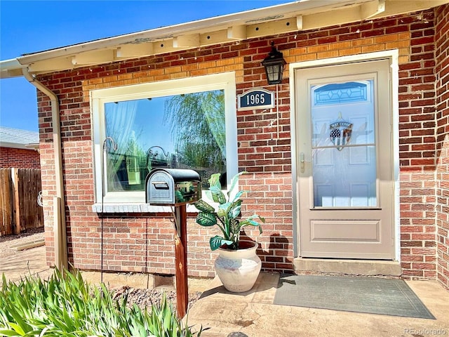 entrance to property featuring brick siding and fence