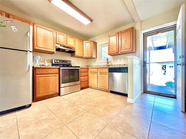 kitchen featuring appliances with stainless steel finishes, light brown cabinets, baseboards, light tile patterned floors, and under cabinet range hood