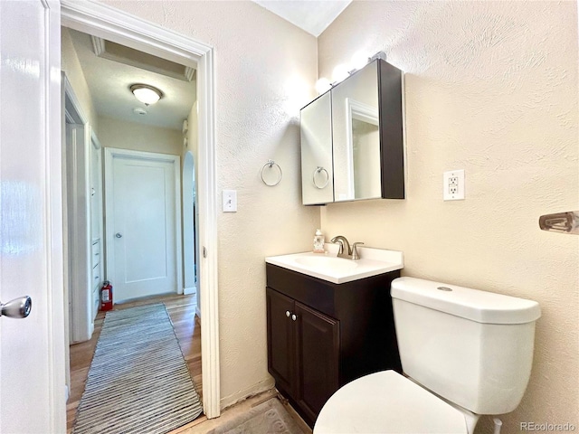 bathroom with toilet, a textured wall, wood finished floors, and vanity