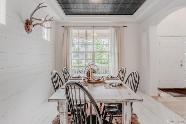 8367 Devinney St, Arvada, CO 80005 - dining space featuring a tray ceiling, arched walkways, light wood-type flooring, wood walls, and baseboards