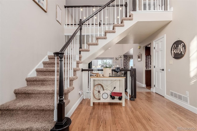 staircase with visible vents, a high ceiling, baseboards, and wood finished floors