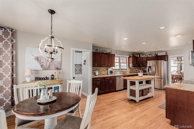 kitchen featuring dark brown cabinetry, light wood-type flooring, decorative backsplash, an inviting chandelier, and stainless steel appliances