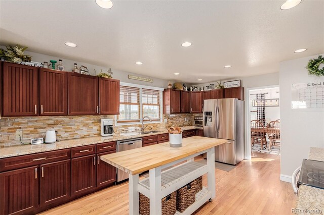 kitchen with a sink, backsplash, light wood-style floors, and appliances with stainless steel finishes