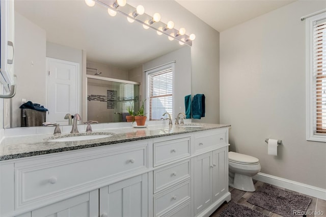 bathroom featuring toilet, a sink, a shower stall, double vanity, and baseboards