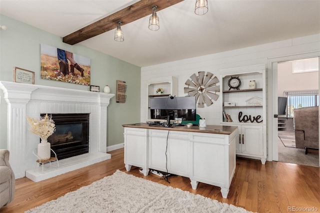 living area with beam ceiling, a brick fireplace, and wood finished floors