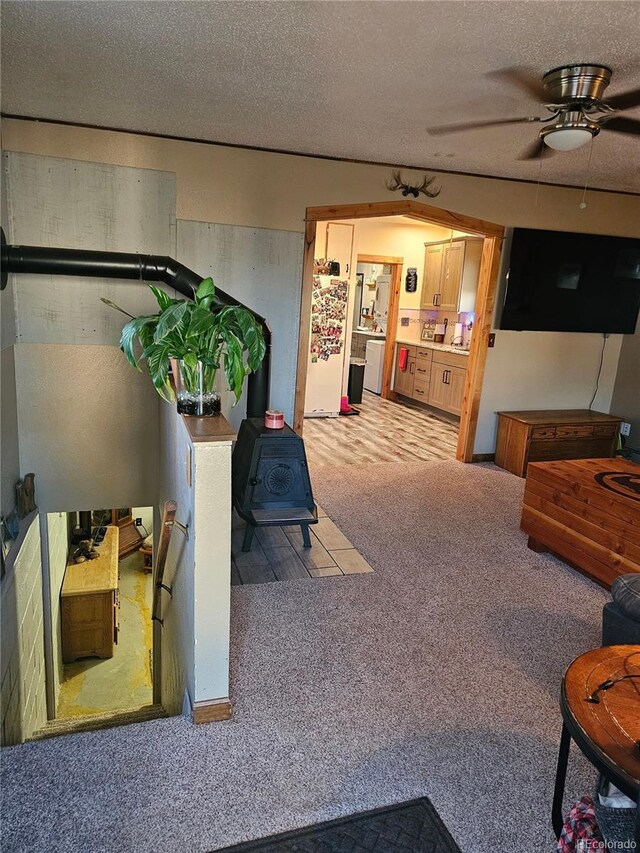 24797 Pleasant Hill Ave, Galeton, CO 80622 - living room featuring a wood stove, ceiling fan, carpet flooring, and a textured ceiling