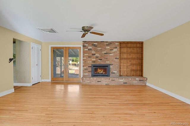 unfurnished living room with built in shelves, ceiling fan, french doors, a brick fireplace, and light hardwood / wood-style floors