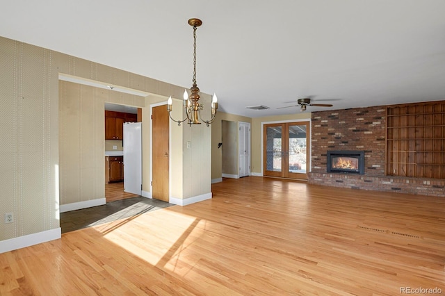 unfurnished living room with hardwood / wood-style flooring, ceiling fan with notable chandelier, a brick fireplace, and french doors