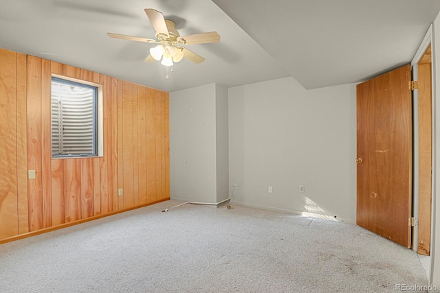 spare room with light carpet, ceiling fan, and wood walls