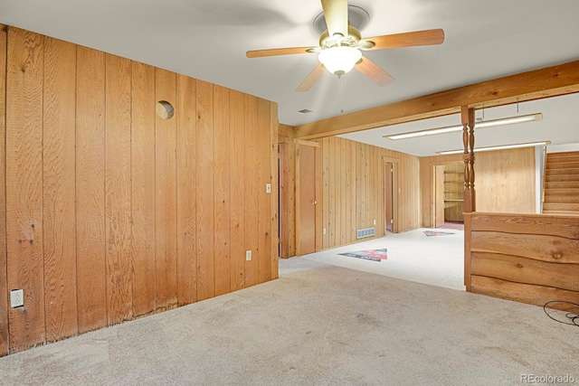 unfurnished room featuring wooden walls, beamed ceiling, light colored carpet, and ceiling fan