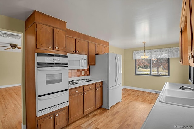 kitchen featuring white appliances, sink, tasteful backsplash, decorative light fixtures, and light hardwood / wood-style floors