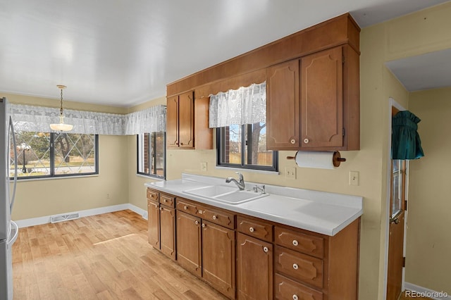 kitchen featuring light hardwood / wood-style flooring, hanging light fixtures, stainless steel refrigerator, and sink