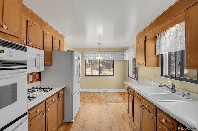 kitchen featuring white appliances, light hardwood / wood-style flooring, hanging light fixtures, and sink