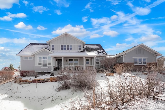 snow covered rear of property with board and batten siding and covered porch
