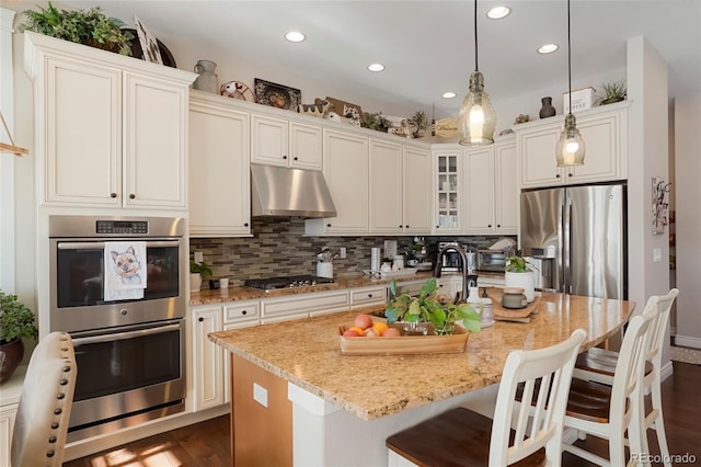 kitchen featuring decorative backsplash, recessed lighting, under cabinet range hood, light stone counters, and stainless steel appliances
