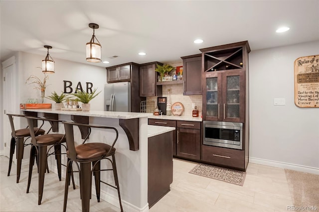 kitchen featuring dark brown cabinets, appliances with stainless steel finishes, decorative backsplash, and a kitchen bar