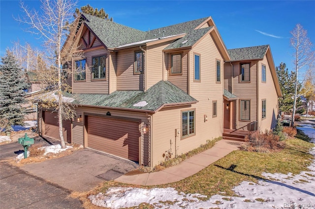 chalet / cabin featuring a shingled roof, an attached garage, and aphalt driveway