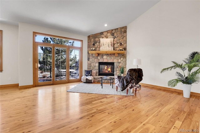 living room with baseboards, a fireplace, vaulted ceiling, and light wood finished floors