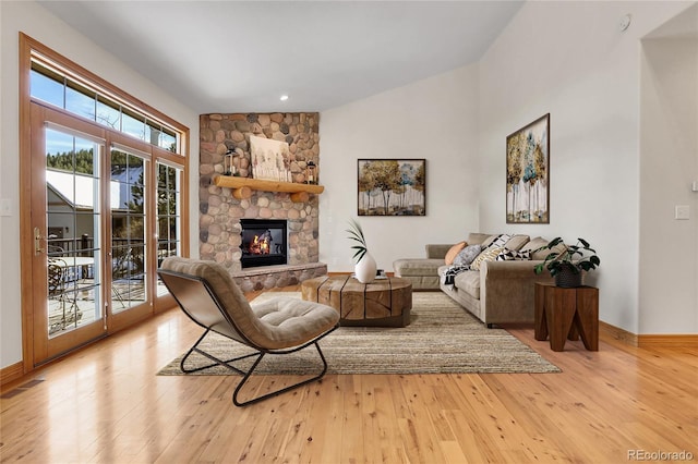 living area featuring light wood finished floors, visible vents, baseboards, and a stone fireplace