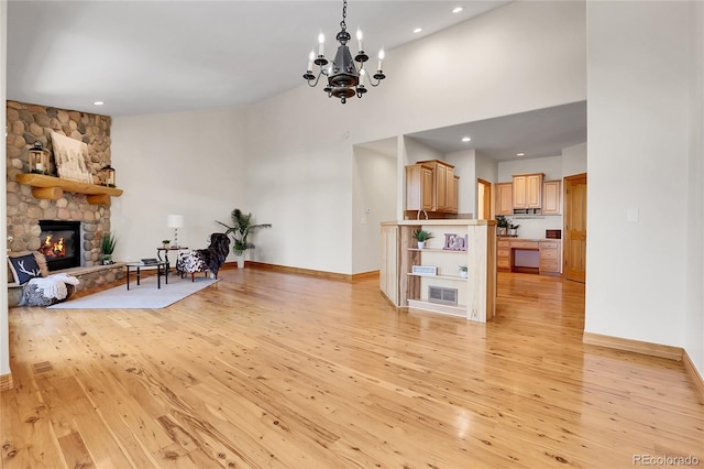 living room featuring a high ceiling, a fireplace, light wood-style flooring, and baseboards