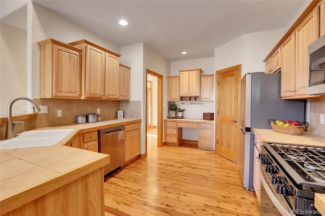 kitchen with light brown cabinets, stainless steel appliances, a sink, light wood-type flooring, and built in study area