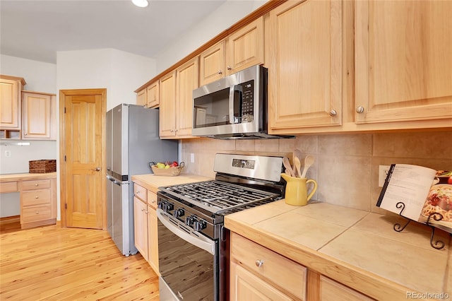 kitchen with tile countertops, light brown cabinets, light wood-style flooring, stainless steel appliances, and decorative backsplash