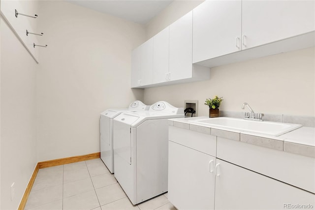 washroom with light tile patterned floors, cabinet space, washing machine and dryer, a sink, and baseboards