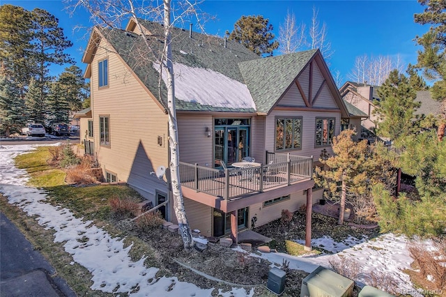 snow covered rear of property featuring a deck and roof with shingles