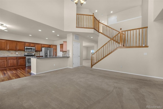 kitchen with a high ceiling, backsplash, kitchen peninsula, carpet, and appliances with stainless steel finishes