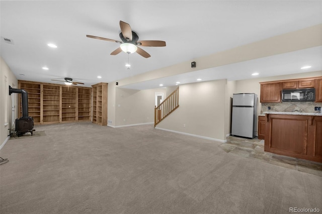 unfurnished living room with ceiling fan, a wood stove, and light carpet