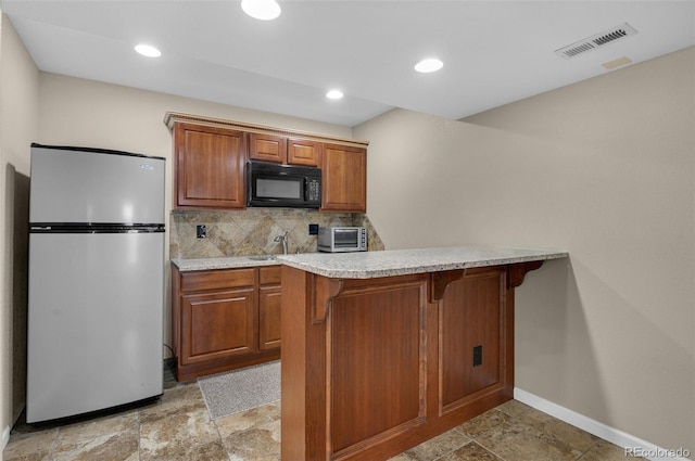 kitchen featuring sink, decorative backsplash, stainless steel fridge, kitchen peninsula, and a breakfast bar area