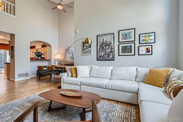 8300 Fairmount Dr Unit Aa102, Denver, CO 80247 - living room featuring arched walkways, a ceiling fan, light wood-style flooring, a towering ceiling, and baseboards
