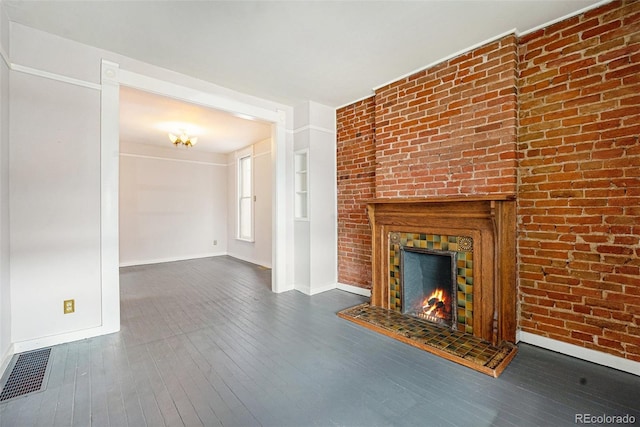 unfurnished living room with dark wood-type flooring, brick wall, and a brick fireplace