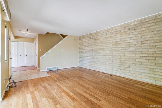 unfurnished living room featuring brick wall, wood finished floors, baseboards, and stairs