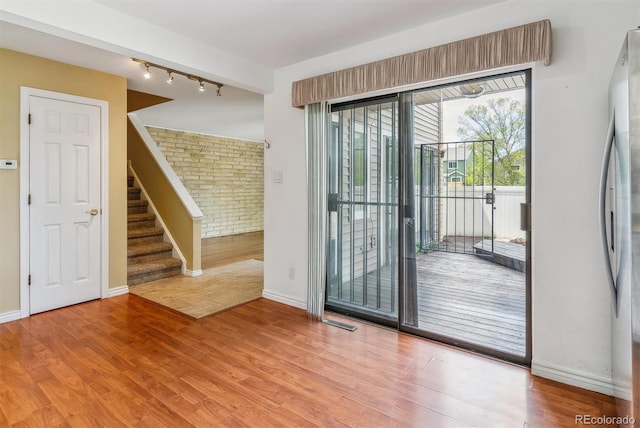 entryway with track lighting, wood finished floors, baseboards, brick wall, and stairway