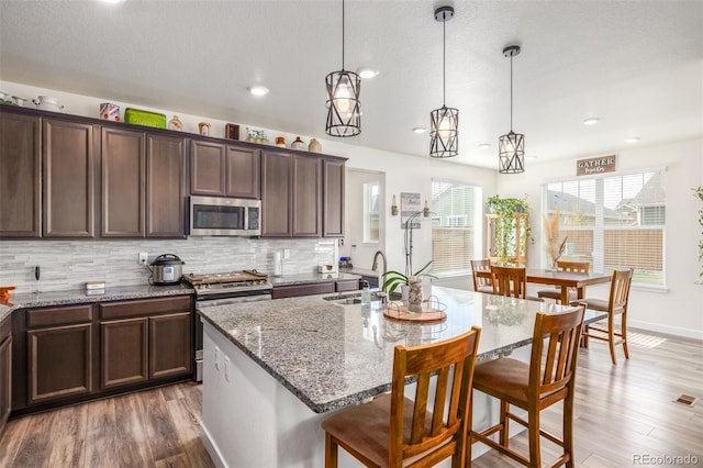 kitchen featuring a center island with sink, appliances with stainless steel finishes, dark hardwood / wood-style floors, and hanging light fixtures