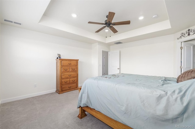 bedroom featuring a raised ceiling, light carpet, and ceiling fan