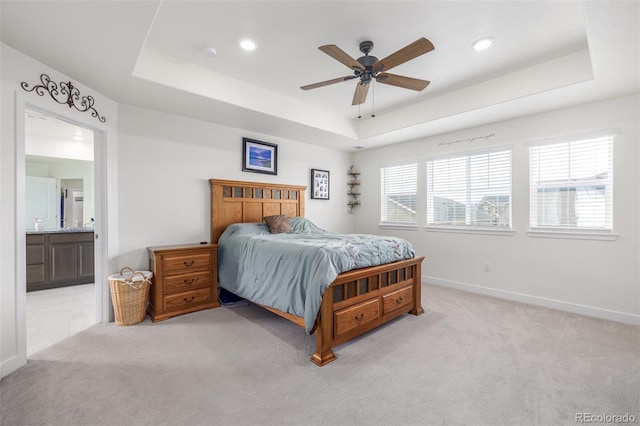 carpeted bedroom featuring a tray ceiling, connected bathroom, and ceiling fan