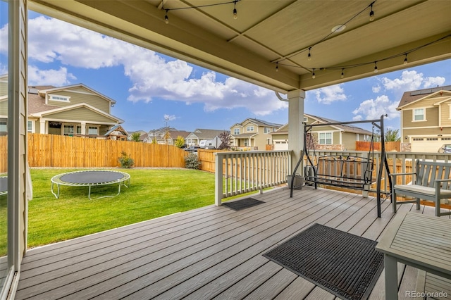 wooden terrace with a trampoline, a lawn, and a garage