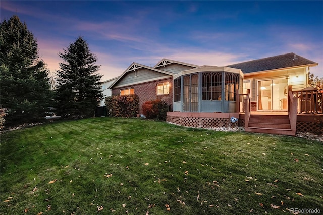 back house at dusk featuring a wooden deck, a sunroom, and a lawn