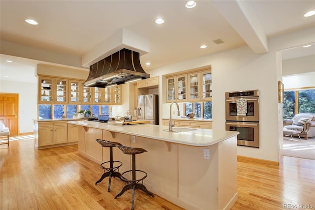 kitchen featuring premium range hood, an island with sink, beam ceiling, appliances with stainless steel finishes, and sink