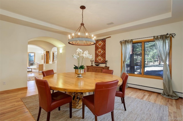 dining area with a baseboard heating unit, a raised ceiling, light hardwood / wood-style flooring, and an inviting chandelier