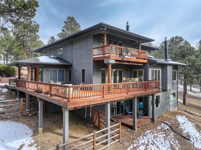 snow covered rear of property featuring a balcony and a wooden deck