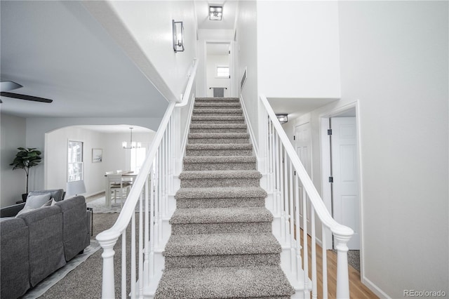 staircase with hardwood / wood-style floors, ceiling fan with notable chandelier, and a high ceiling