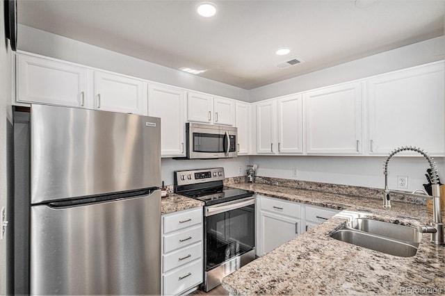 kitchen featuring visible vents, white cabinets, light stone counters, appliances with stainless steel finishes, and a sink